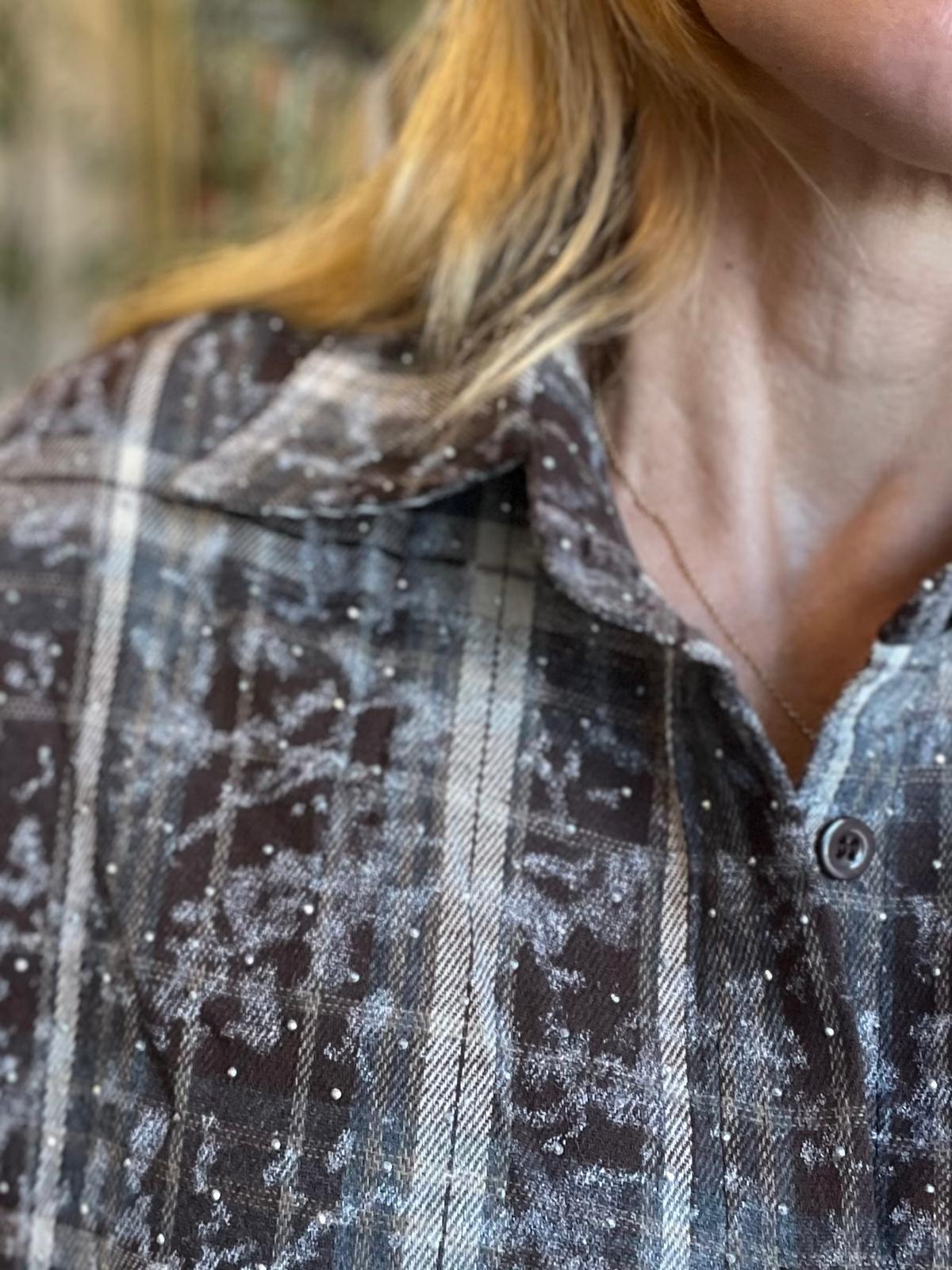 Närbild av en person med blont hår som bär en gråsvart rutig skjorta, beströdd med vita snö- eller frostflingor. Krage och hals syns, med en tunn kedja, mot en suddig utomhusbakgrund.